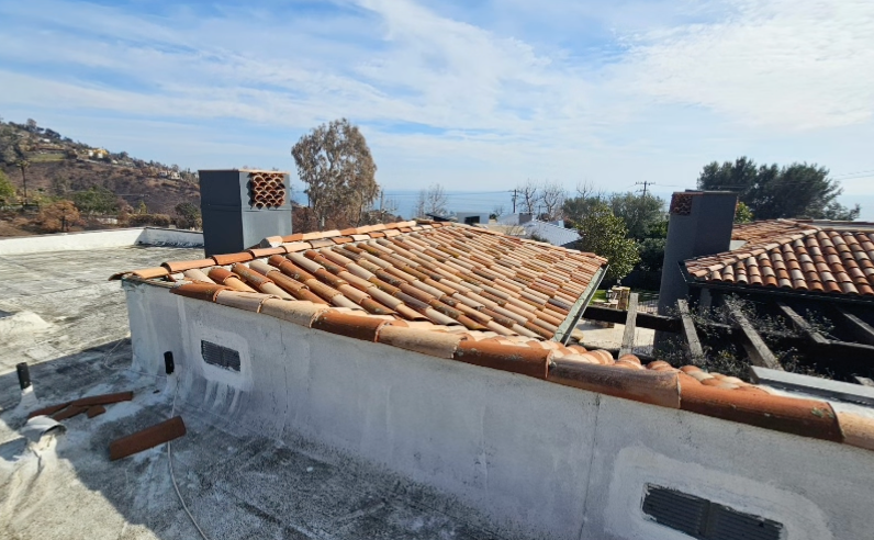 Rooftop with terracotta tiles and white walls, overlooking a rocky hillside and distant sea.