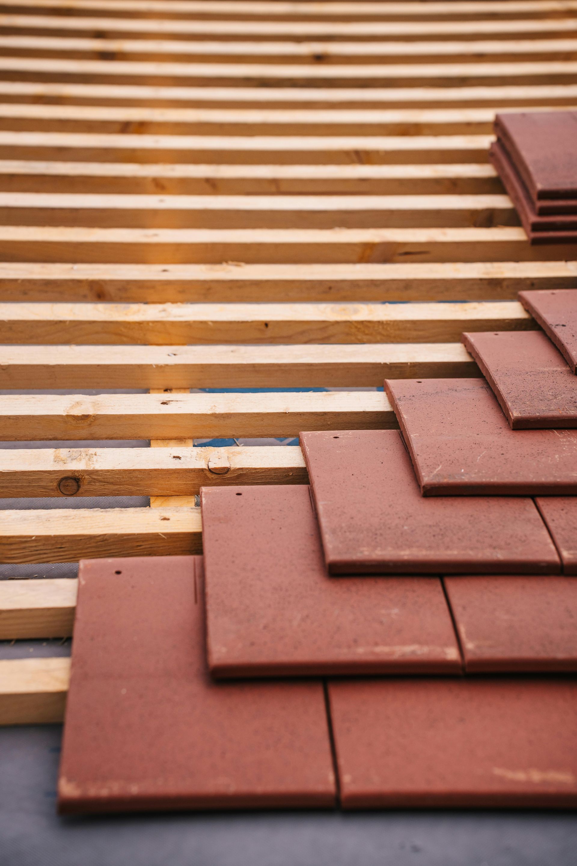 Red roof tiles being laid on wooden rafters.