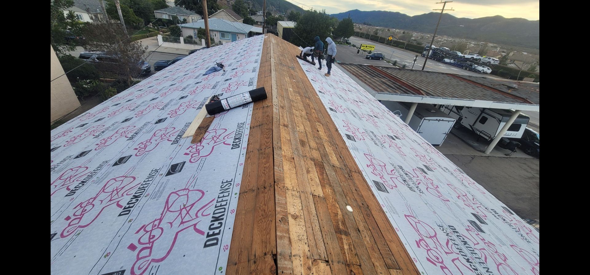 Workers installing roofing material on a house. The roof is partially covered with white underlayment.