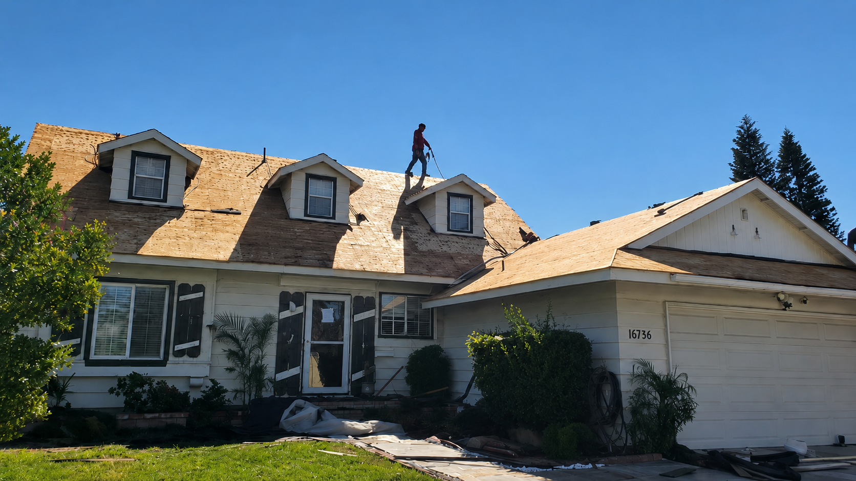 Worker on a roof above a beige house with dormer windows on a sunny day