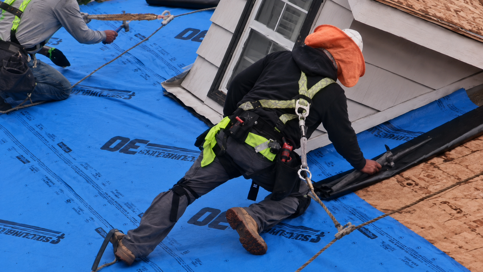 Roofers installing blue waterproof underlayment around a chimney on a sloped roof