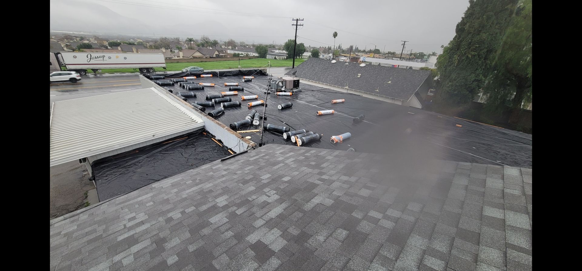 View of a building roof and a flooded parking lot with many cars, overcast day.