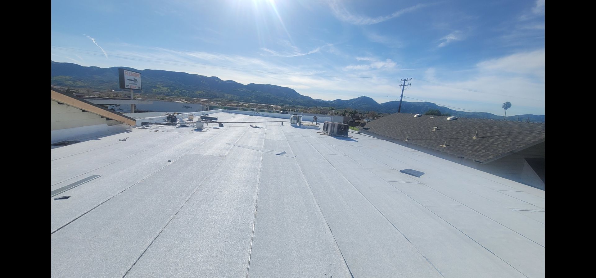 View of a white roof with buildings, mountains, and a clear blue sky.