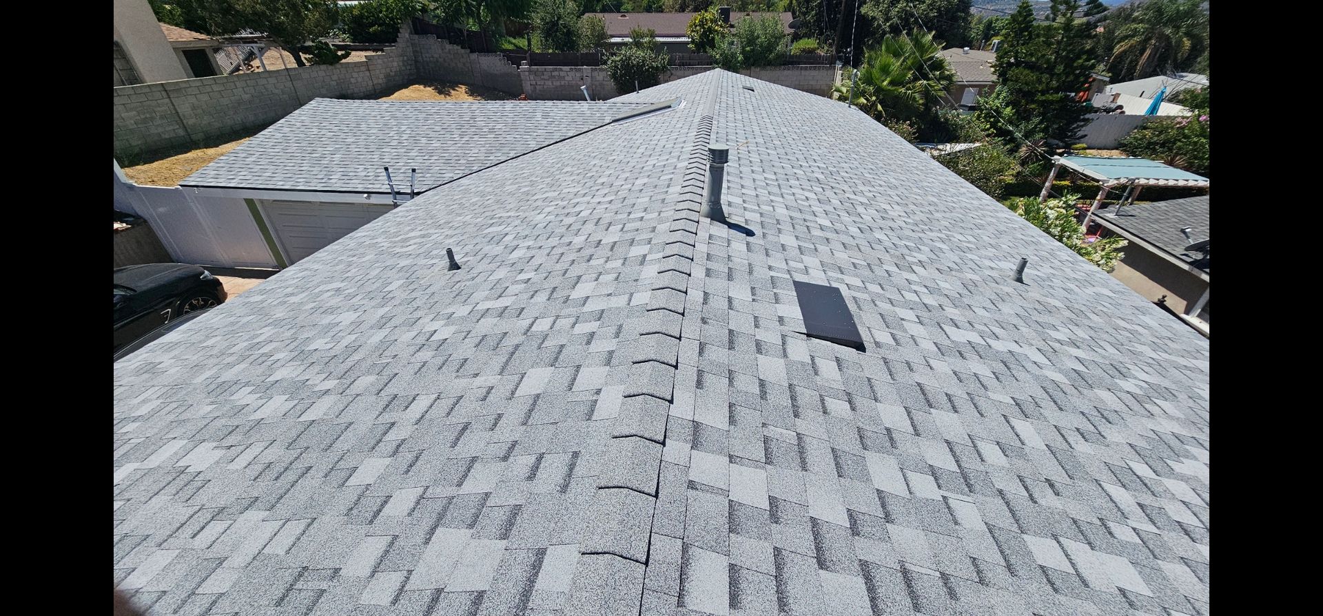 View from above of a gray shingle roof on a house, with a chimney and trees in the background.