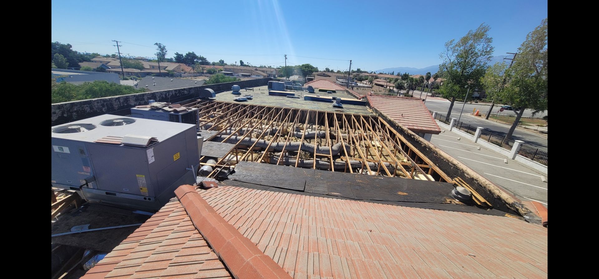 Rooftop view of a partially constructed roof with exposed wooden beams and a blue sky.