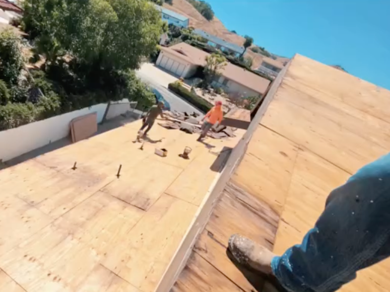 Workers installing a wooden roof on a steep hillside with ocean view in the background