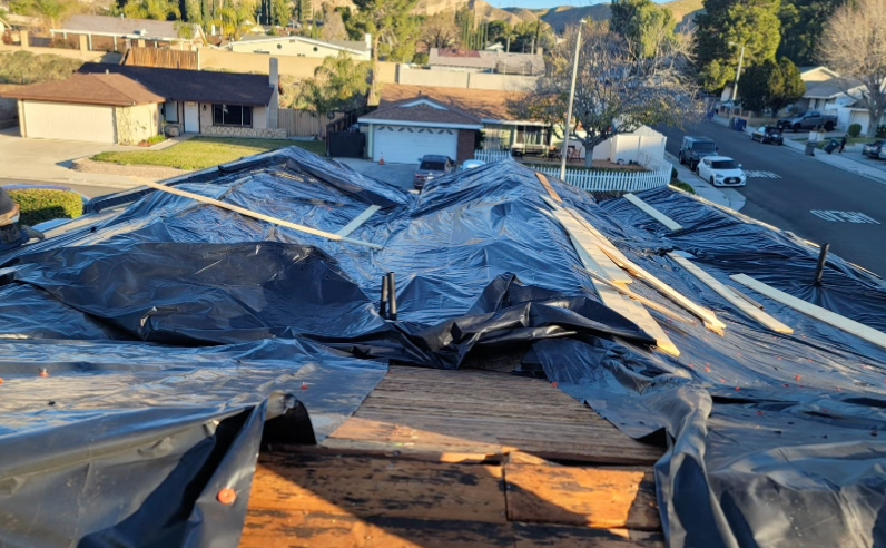 Damaged roof covered with black tarps on a house in a suburban neighborhood