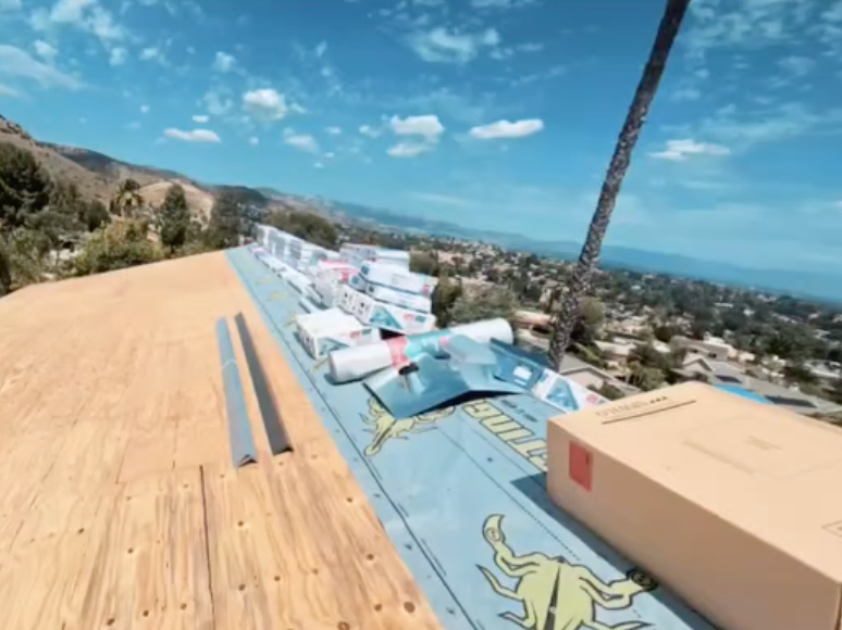 Outdoor rooftop deck with colorful lounge chairs, a large box, and a hillside ocean view under a blue sky