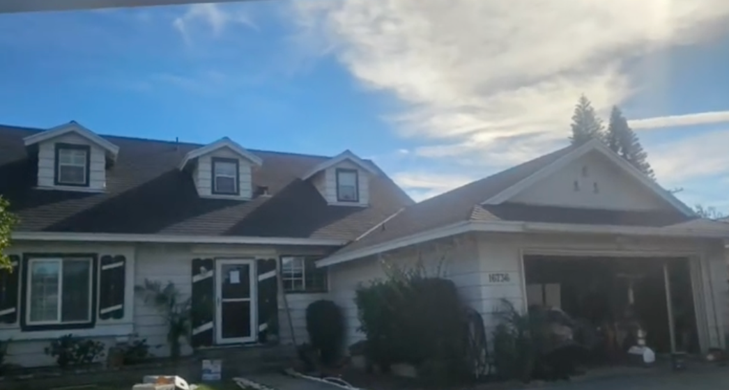 Large house with dormer windows and a covered porch under a bright, cloudy sky