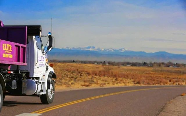 A dump truck is driving down a road with mountains in the background.