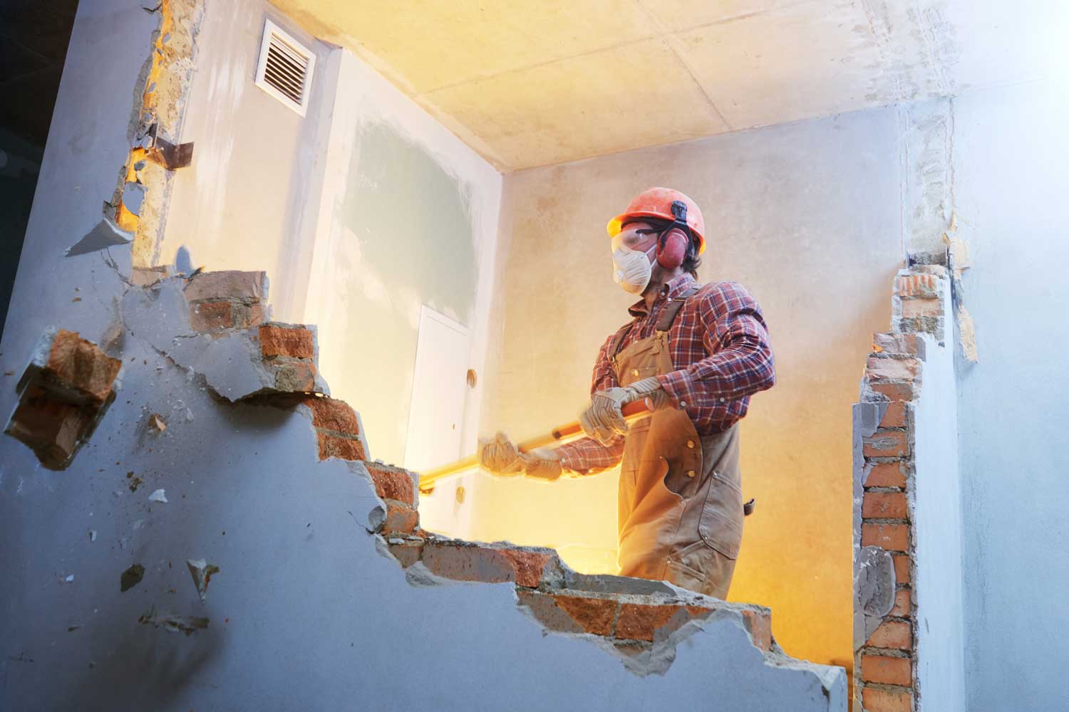 A man is breaking a brick wall with a hammer.