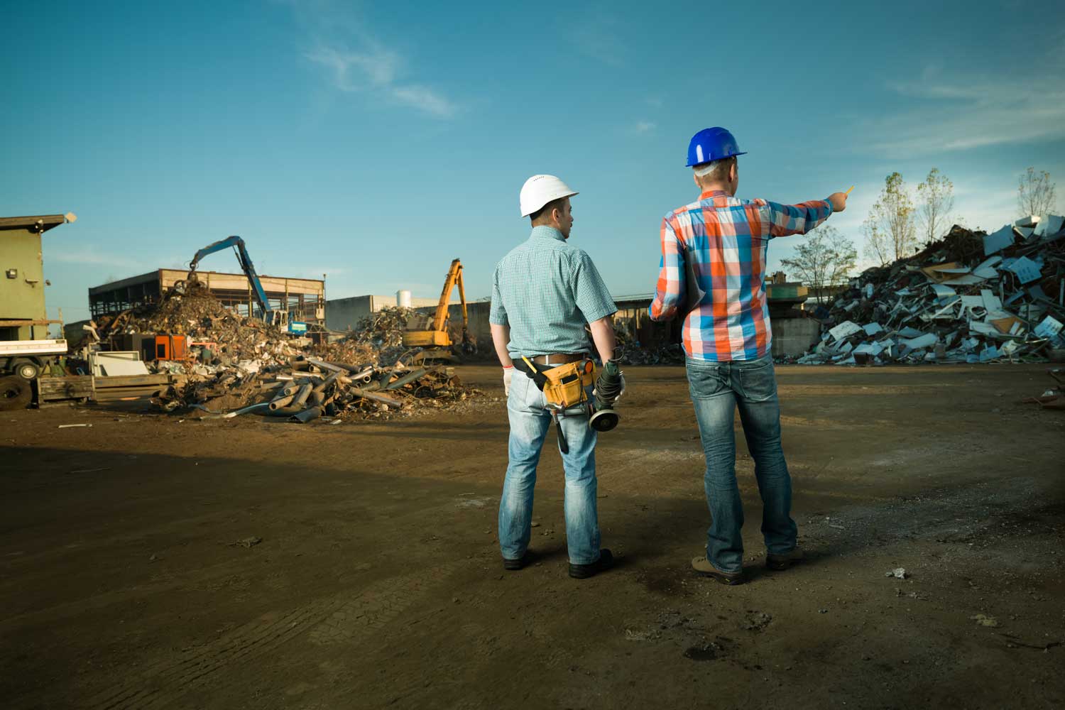 Two construction workers are standing in front of a pile of scrap metal.