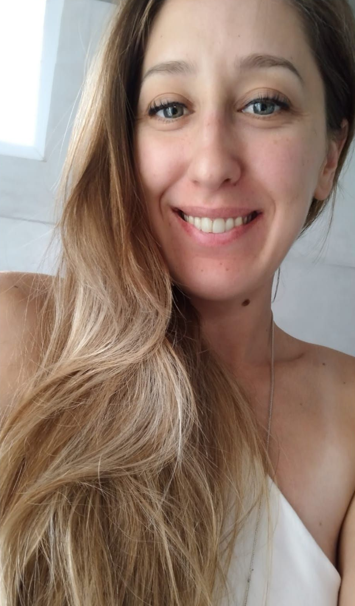 Mujer con cabello largo y rubio sonríe, mirando a la cámara.