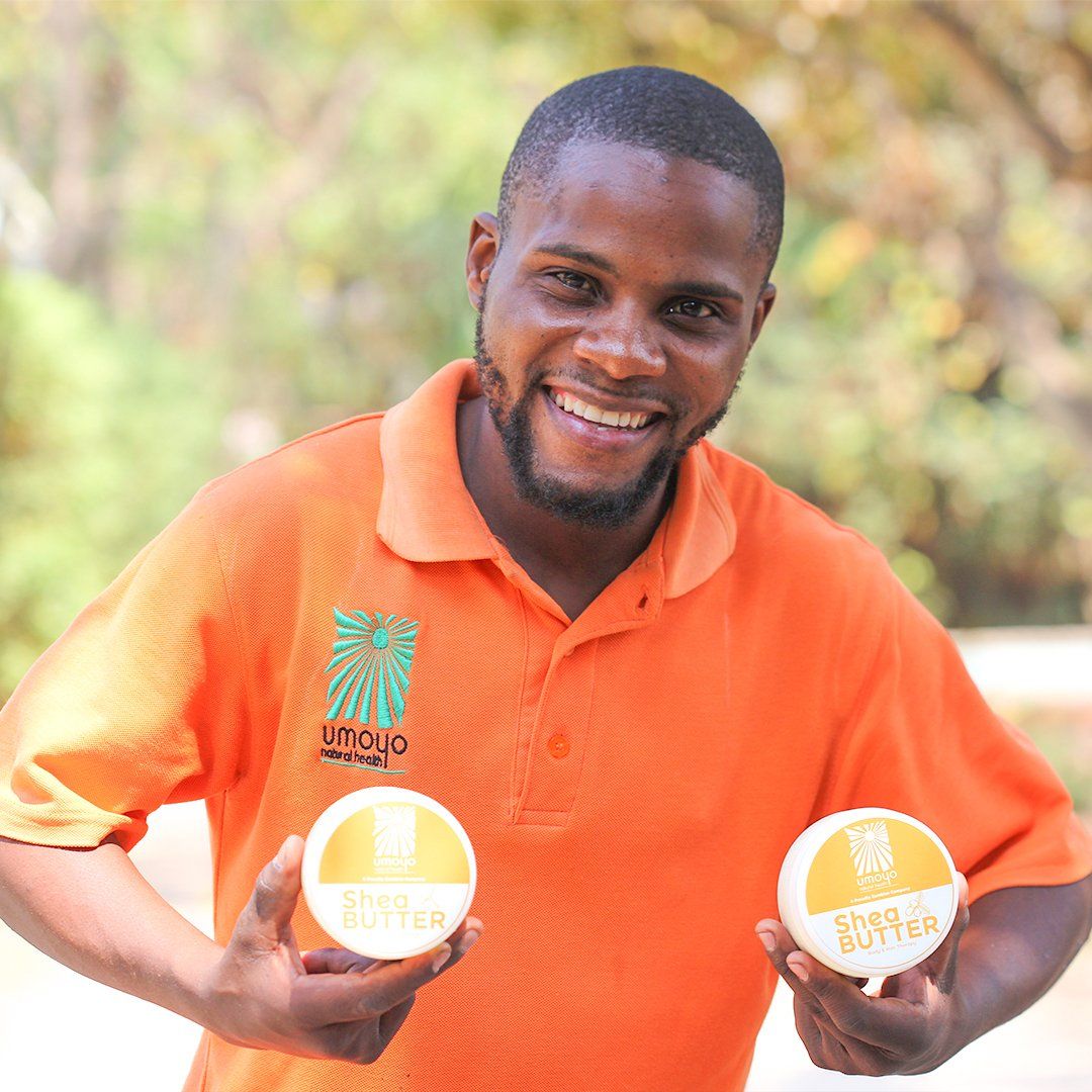 A man in an orange shirt is holding two jars of lotion