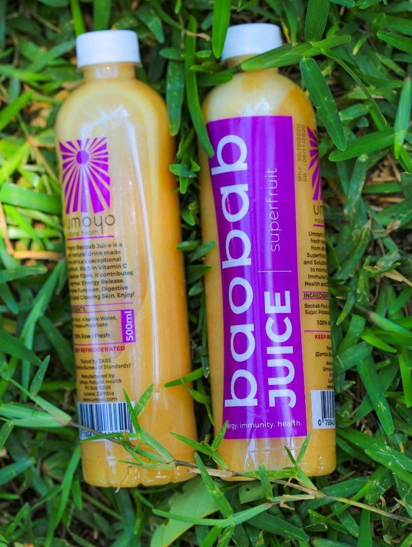 Two bottles of baobab juice are laying in the grass