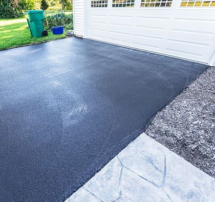 a black asphalt driveway next to a white garage door .