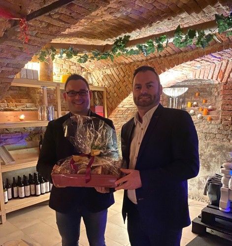 Zwei Männer stehen nebeneinander in einem Weinkeller und halten einen Korb mit Lebensmitteln.