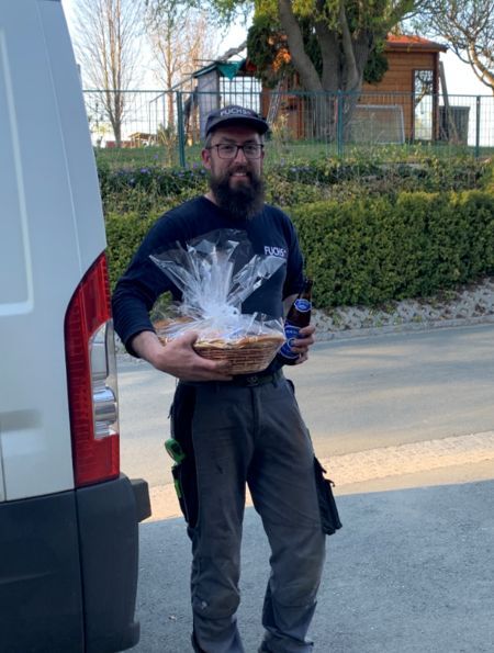 Ein Mann mit Bart hält einen Korb mit Essen und eine Flasche Bier.