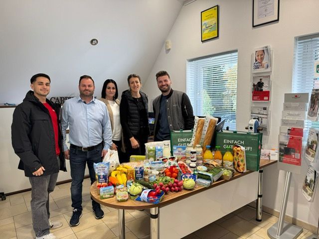 Fünf Personen stehen in einem Raum in der Nähe eines Tisches mit gespendeten Lebensmitteln.