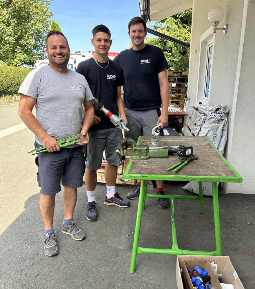 Drei Männer stehen nebeneinander vor einem grünen Tisch.