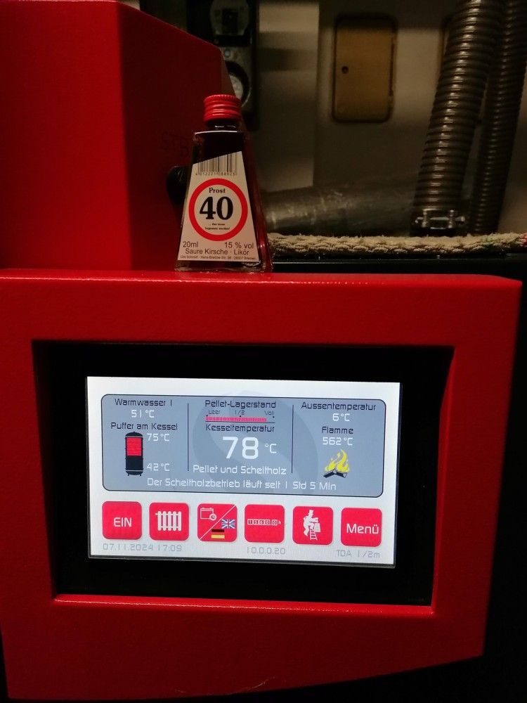 Ein roter Thermostat mit einer Flasche Öl daneben.