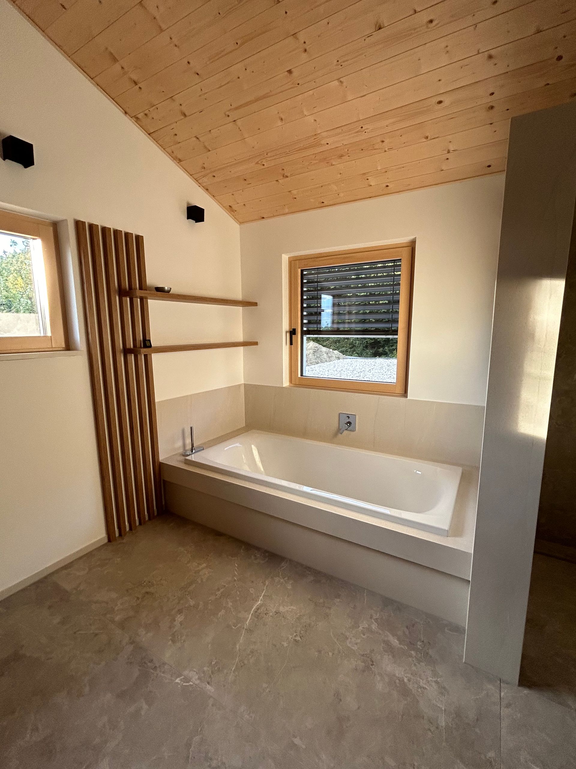 In einem Badezimmer steht eine Badewanne neben einem Fenster.