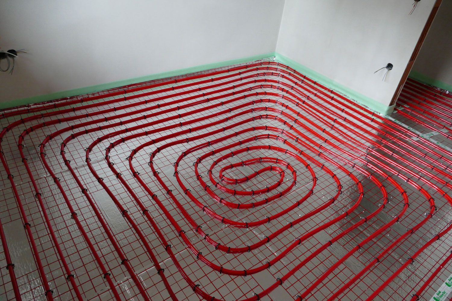 Ein Raum mit einem kreisförmigen Muster aus roten Rohren auf dem Boden für eine Fußbodenheizung.