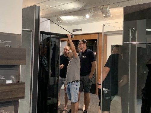 Eine Gruppe Männer steht in einem Raum und schaut sich einen Kühlschrank an.