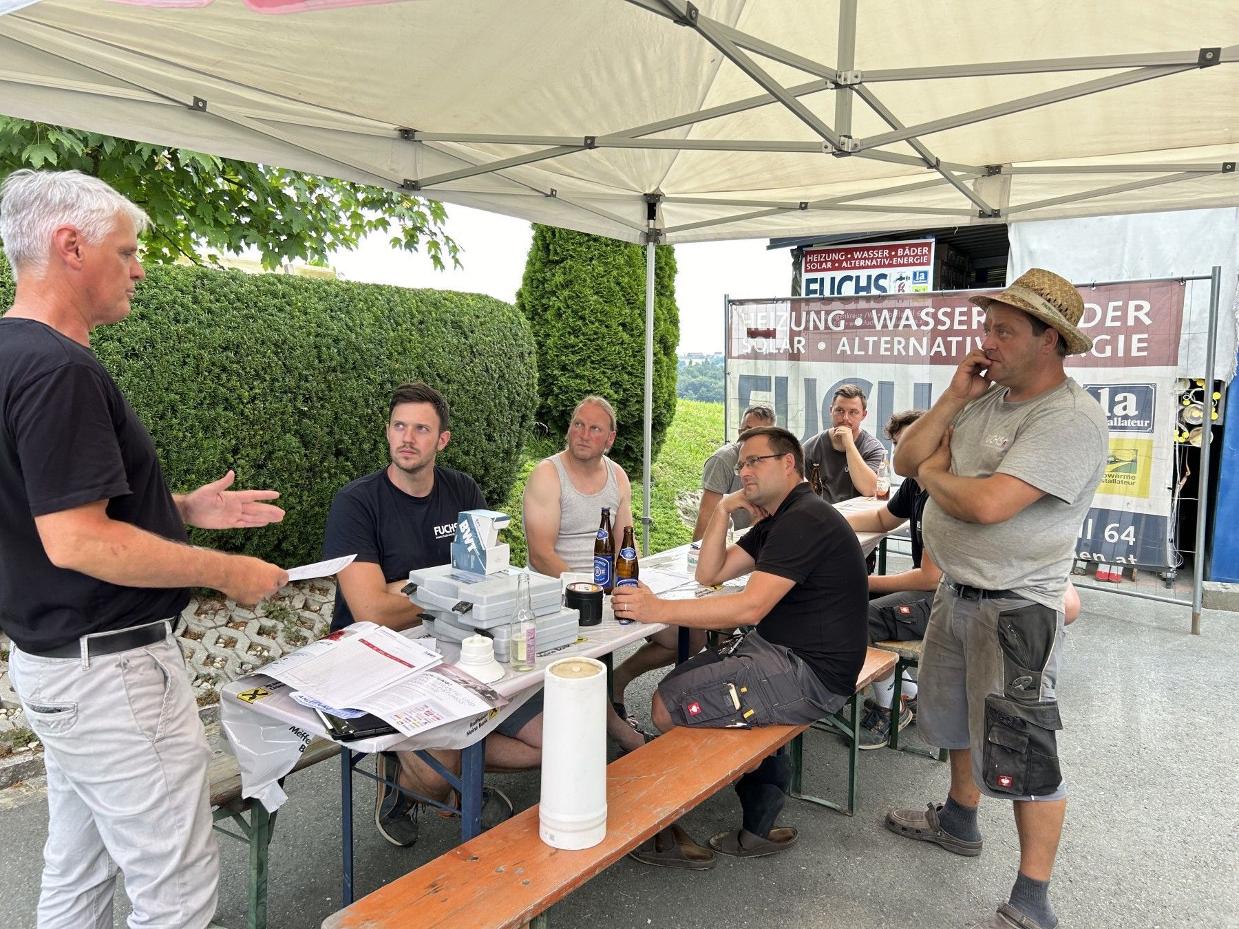 Eine Gruppe Männer sitzt an Tischen unter einem Zelt.