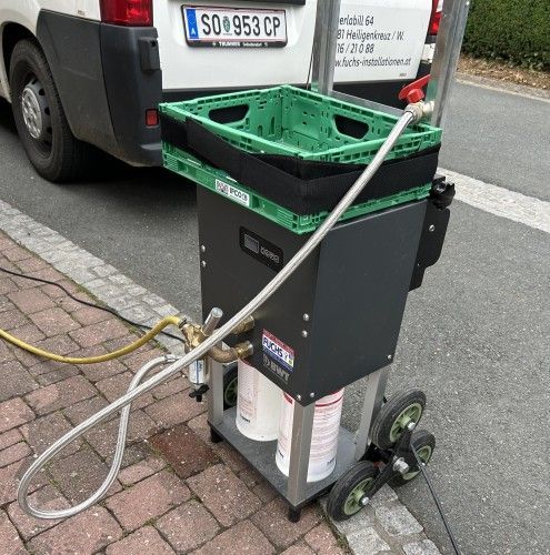 Auf einem Karren neben einem weißen Lieferwagen steht eine grüne Kiste.