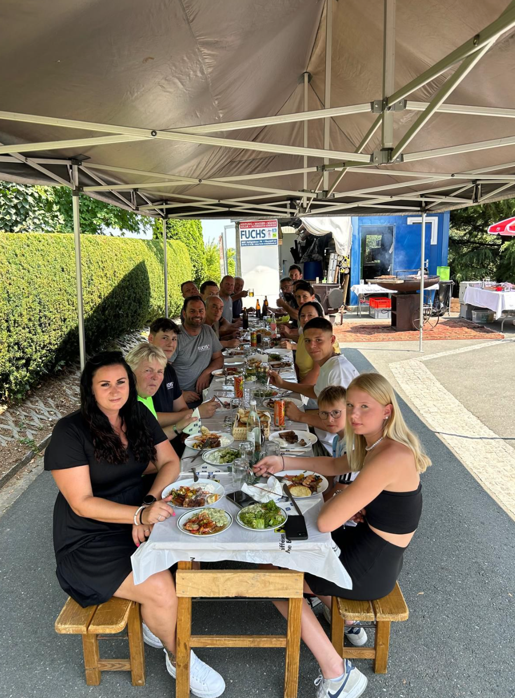 Eine Gruppe von Menschen sitzt an einem langen Tisch unter einem Zelt.