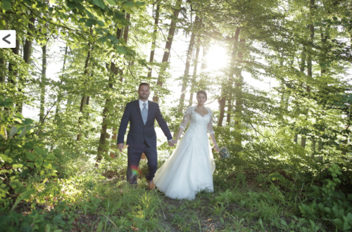 Eine Braut und ein Bräutigam gehen Hand in Hand durch den Wald.