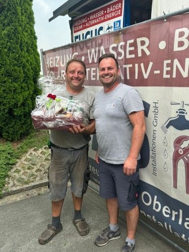 Zwei Männer stehen nebeneinander vor einem Schild mit Geschenken.