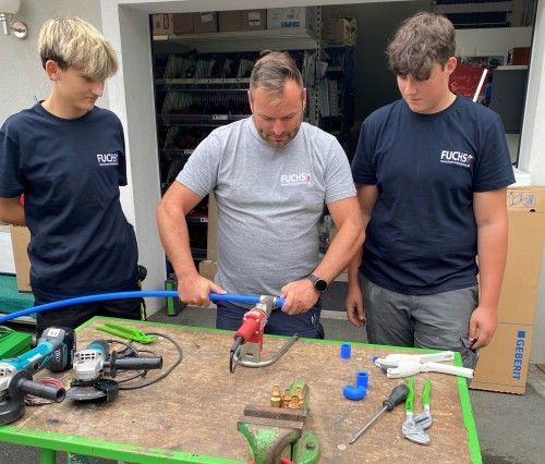 Drei Männer stehen um einen Tisch herum, auf dem Werkzeuge liegen.
