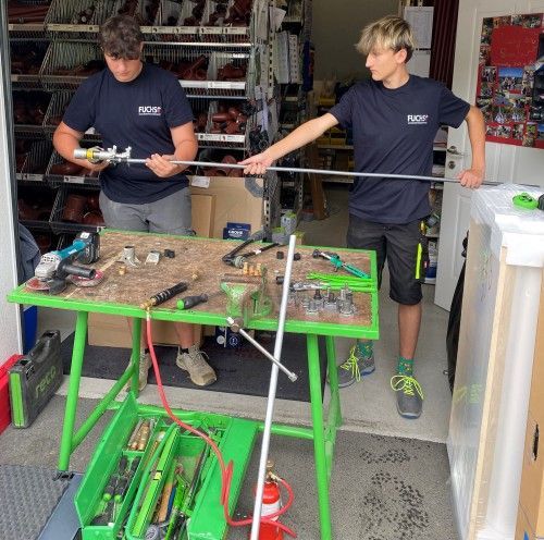 Zwei Männer stehen neben einem grünen Tisch mit Werkzeugen darauf.