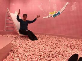 A woman is sitting on a slide in a room filled with pink beans.