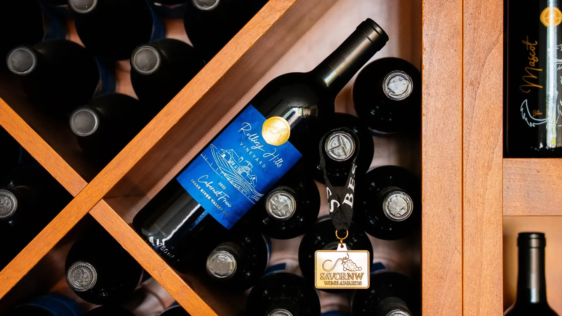 Wine bottles stored in a wooden rack; one bottle with a blue label is in focus.