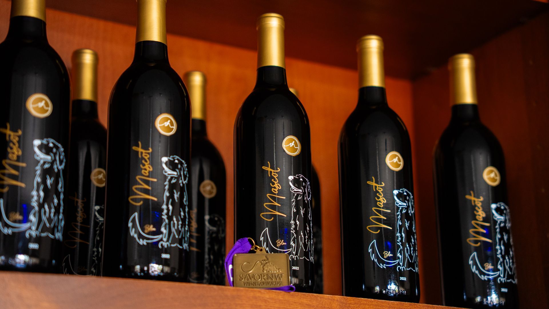 Wine bottles with gold foil tops and labels on a wooden shelf.