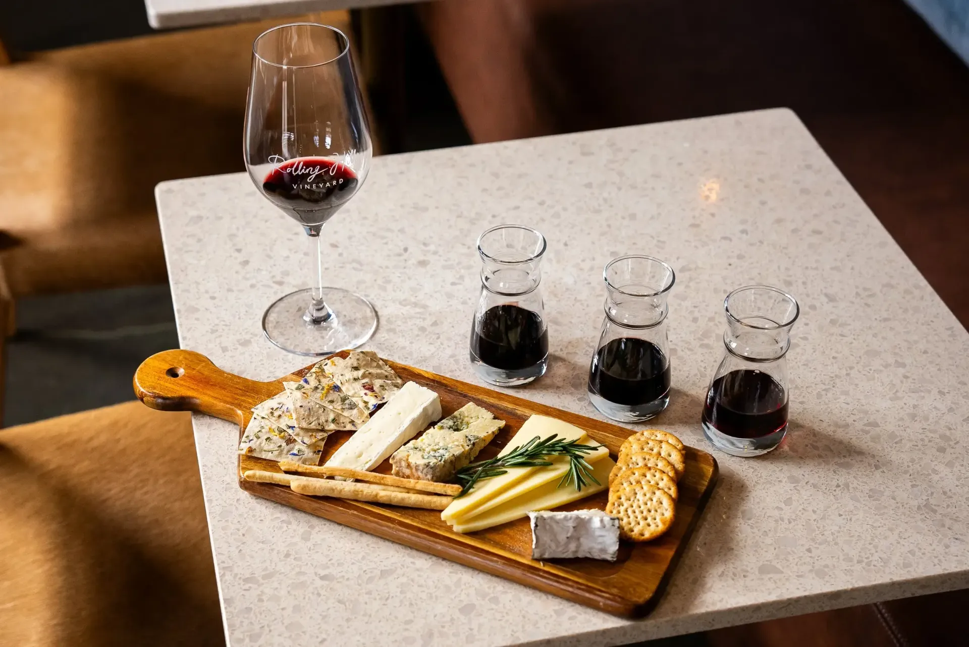 Wine glass with red wine, cheese board, and three small wine glasses on a table.