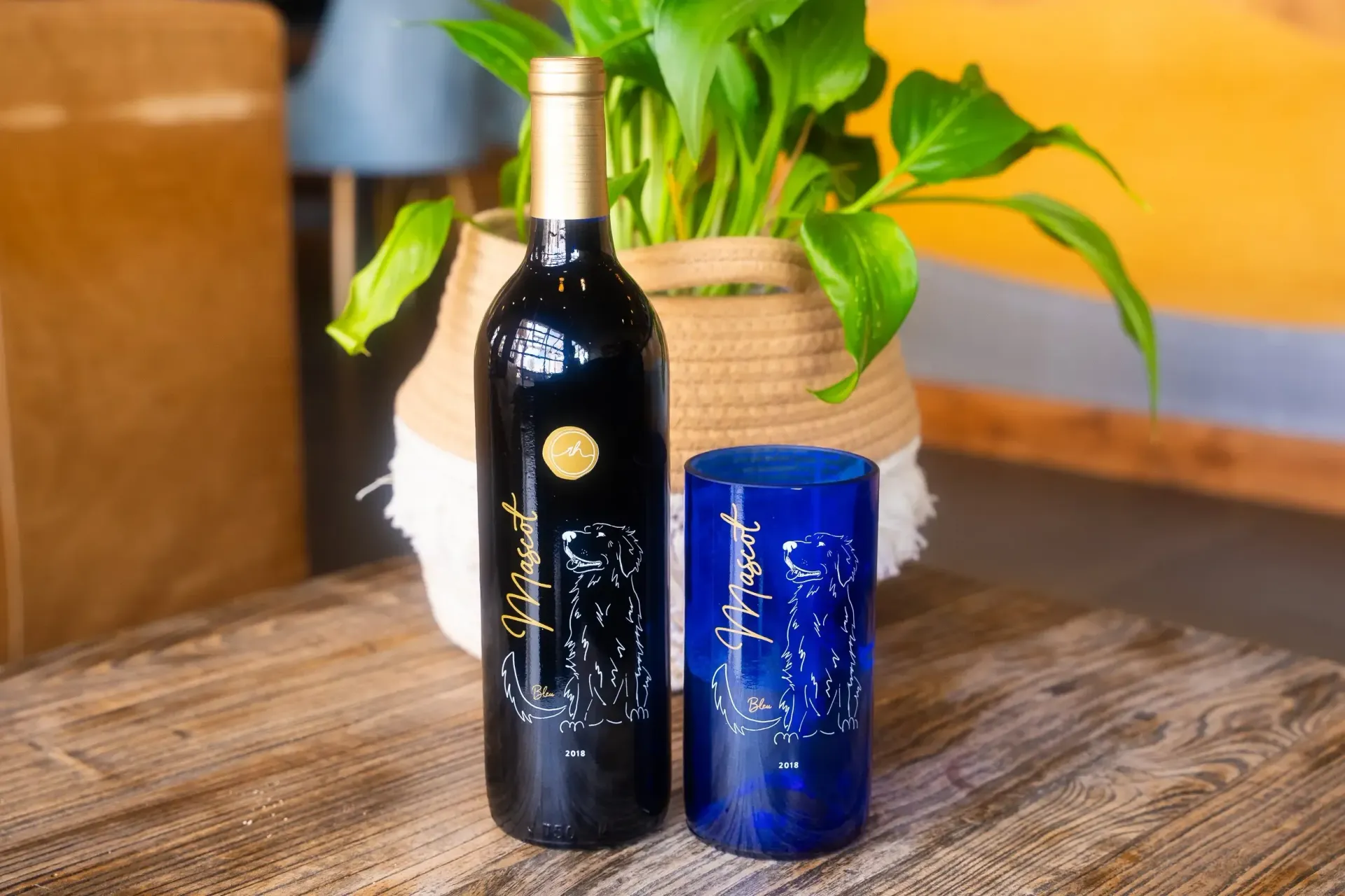 A wine bottle and blue glass next to a potted plant on a wooden table.