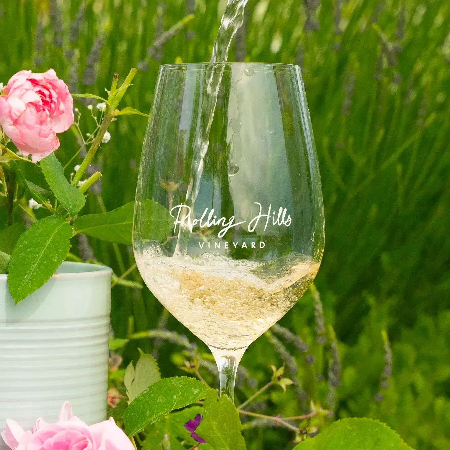 Wine being poured into a glass, with pink roses and lavender in the background.