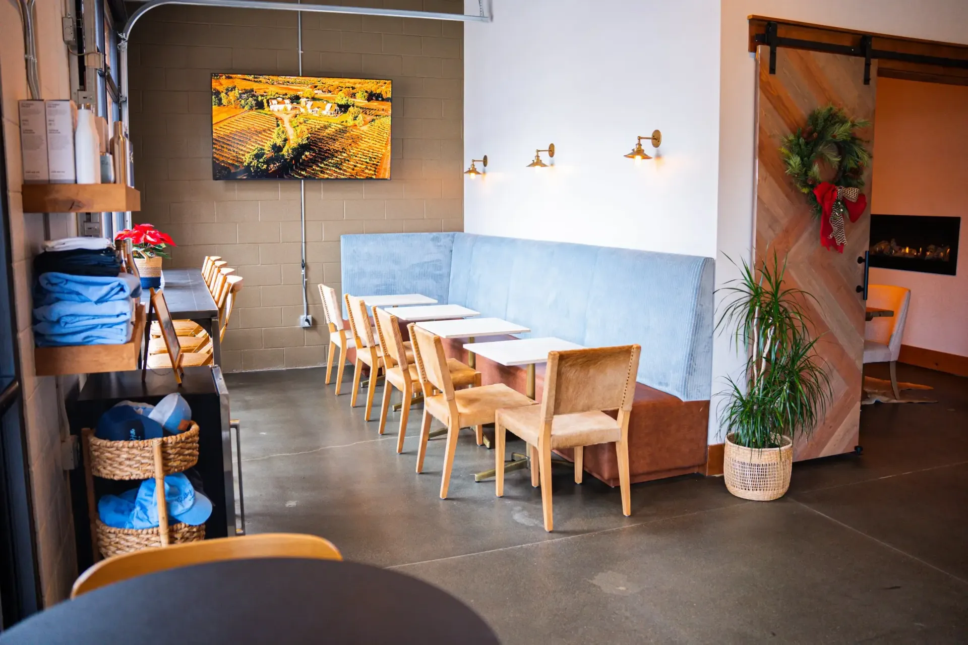 Interior of a cafe with a long blue booth, small tables, wooden chairs, and a sliding wooden door.