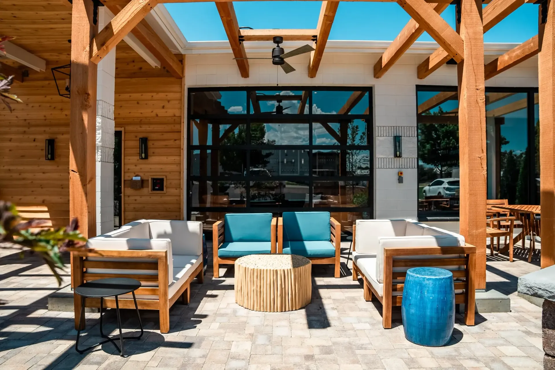 Outdoor patio with seating: wooden beams, white walls, glass doors, blue and tan furniture.