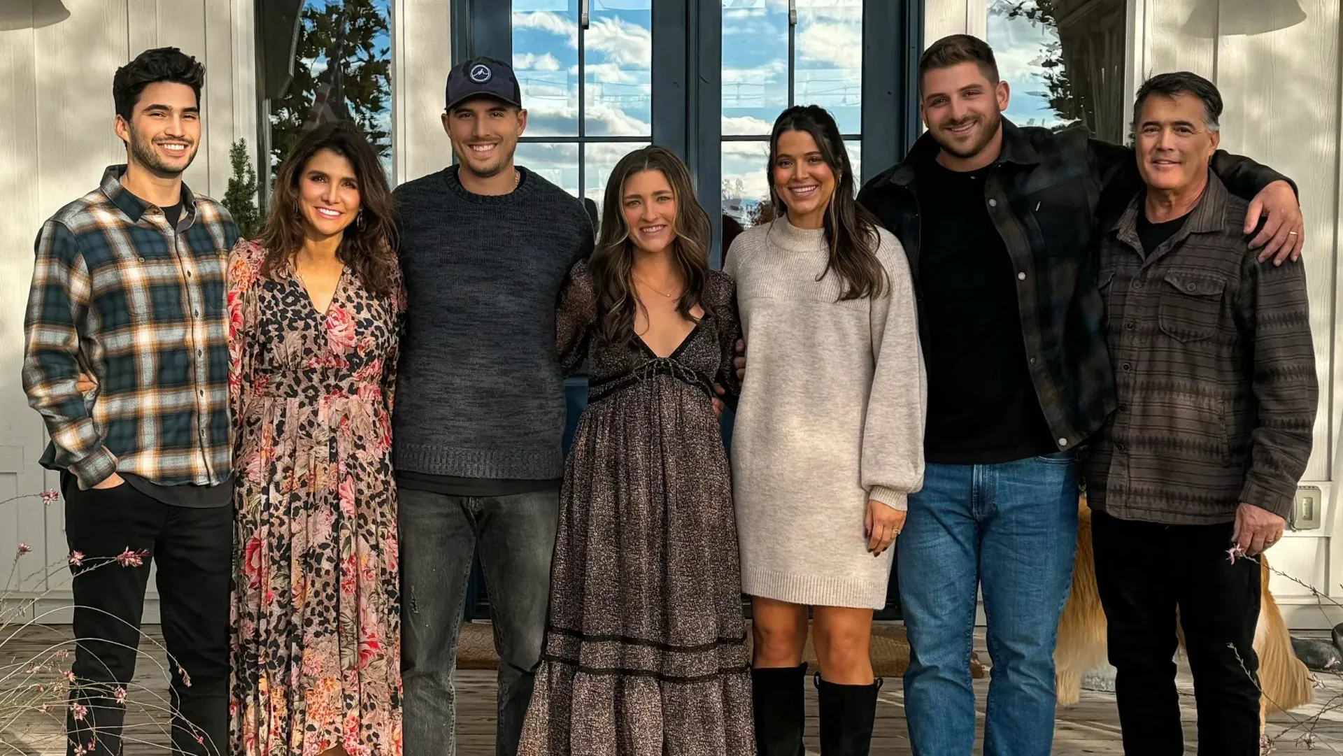 Group of seven people smiling, posing together outside a white building.