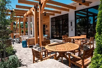 Outdoor patio with wooden furniture, pergola, and modern building.