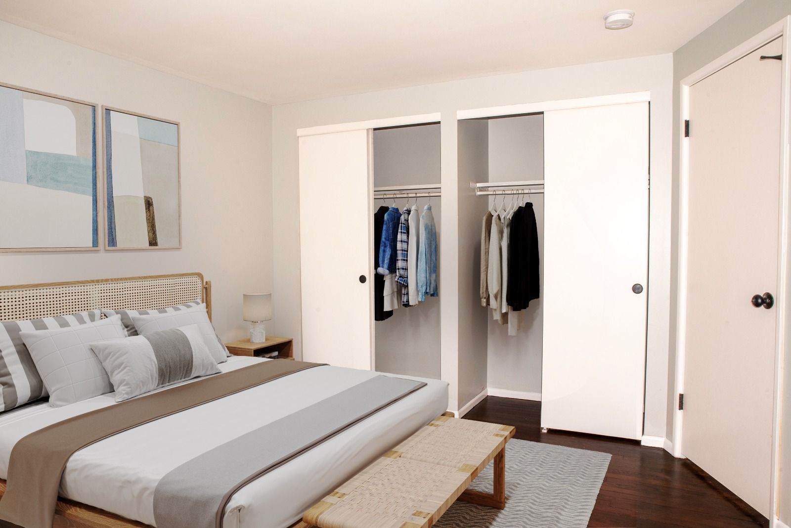 A bedroom with a large bed , closets and a bench.