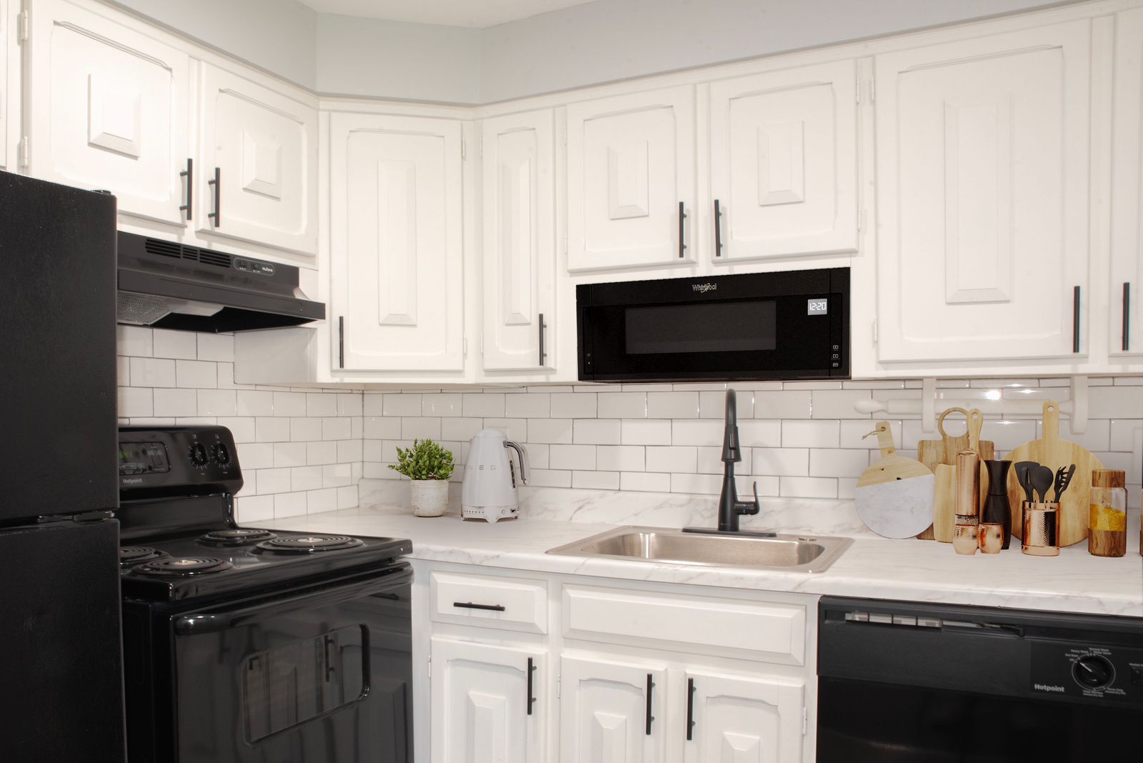 A kitchen with white cabinets , black appliances , a sink , stove and microwave.