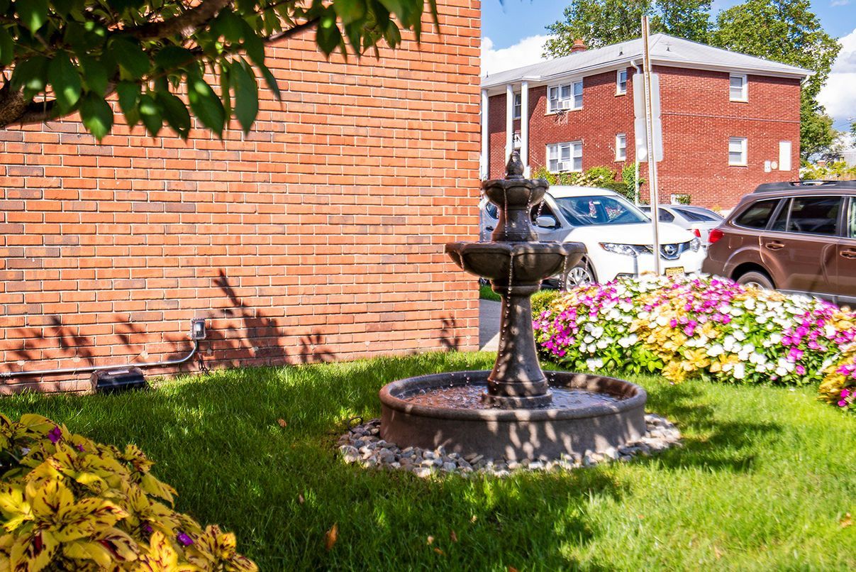 Outdoor courtyard with a brick wall, fountain, and flower beds beside parked cars. Ready to make Joralemon your home? Contact us today to learn more about our pet-friendly 1, 2, and 3-bedroom apartments for rent in Belleville, NJ. We can’t wait to welcome you home!