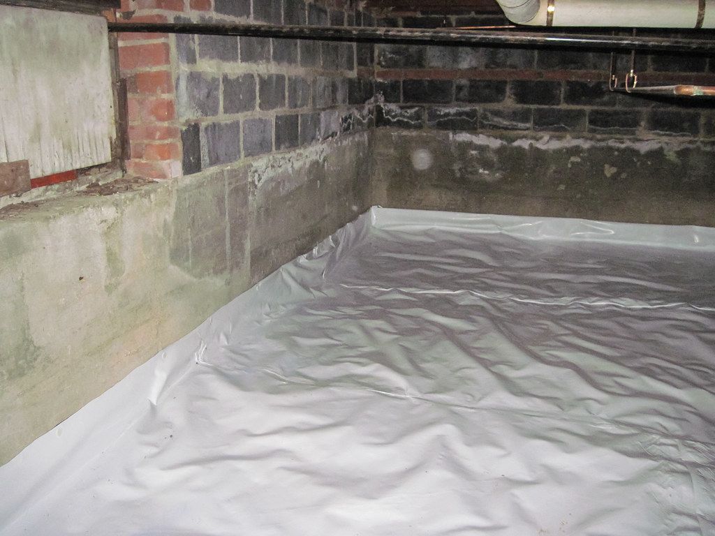 A basement with a white tarp on the floor and a brick wall.