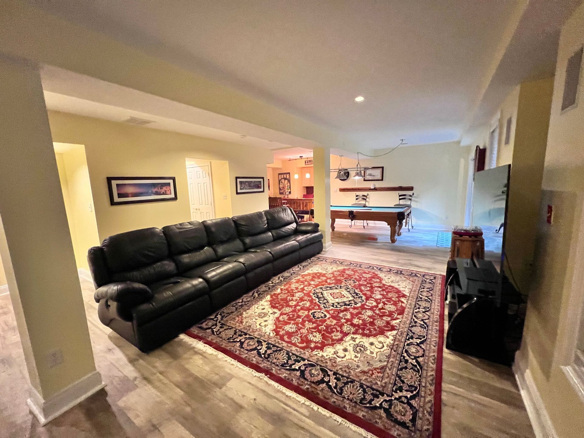 Black leather sofa and Persian rug in a finished basement room with a pool table in the background.